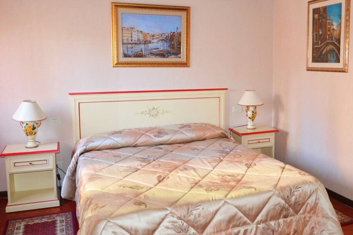 Ein Schlafzimmer mit einem Bett, zwei Nachttischen, zwei Lampen und zwei gerahmten Bildern an der Wand.
