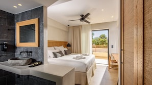 Habitación de hotel moderna con un lavamanos de piedra, una cama grande, un ventilador de techo y vistas al exterior.