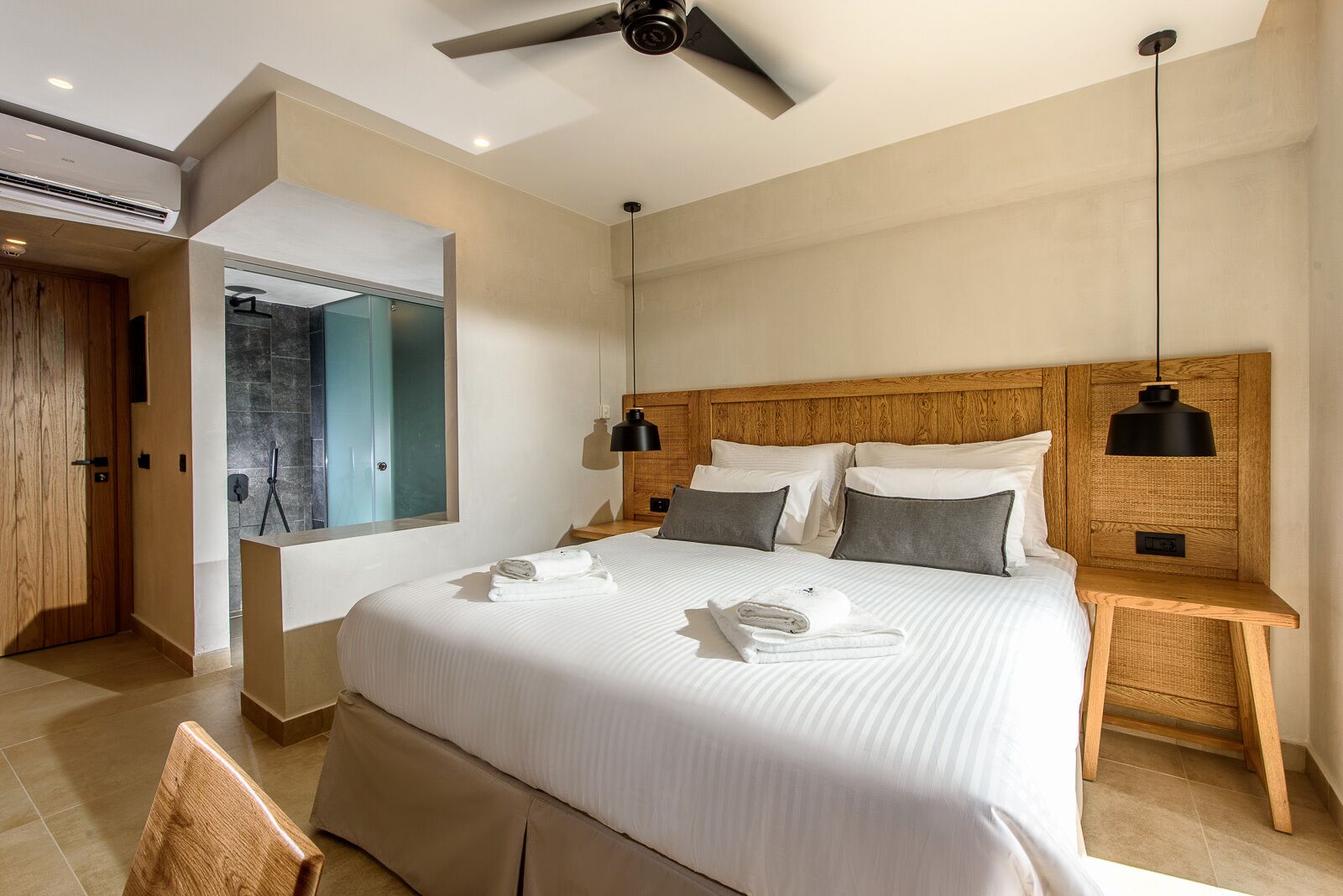 Ein modernes Hotelzimmer mit einem großen Bett, einem Holzkopfende, zwei Nachttischen mit Lampen, einem großen Spiegel und Blick ins Badezimmer.
