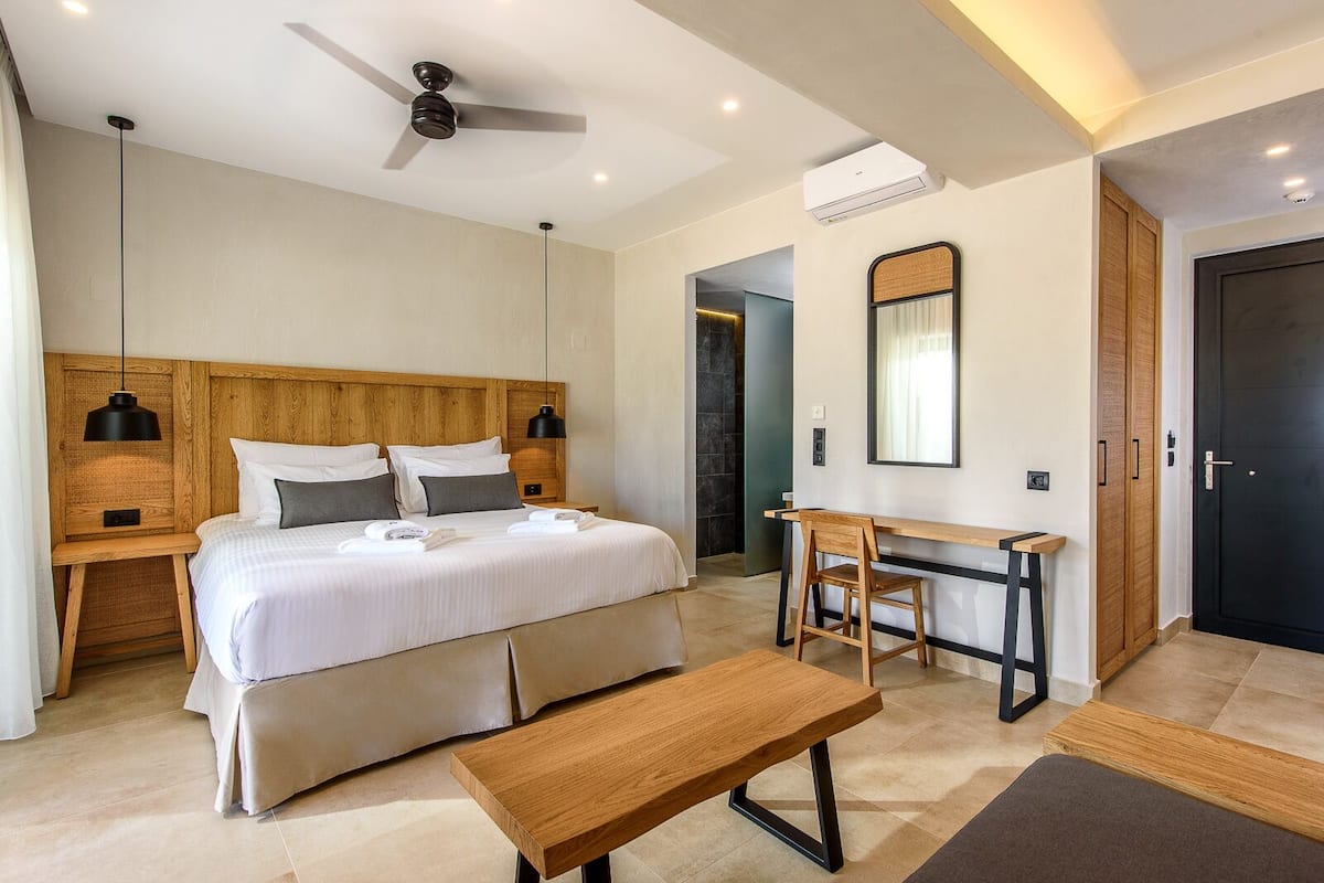 A modern hotel room with a large bed, a desk, a bench, and a ceiling fan.