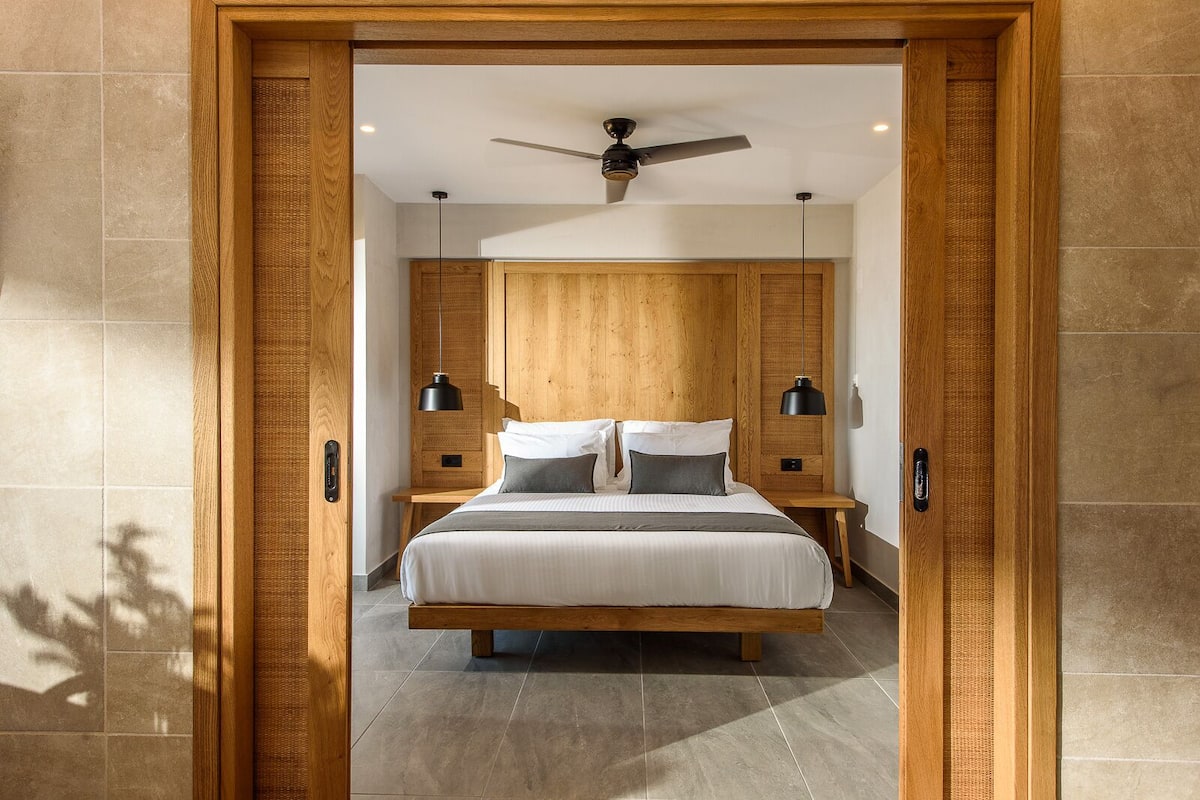A modern bedroom with a wooden headboard, a large bed, two bedside tables, and a ceiling fan.