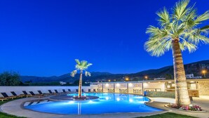 Un área de piscina con sillones de descanso, una palmera y un edificio con terraza.