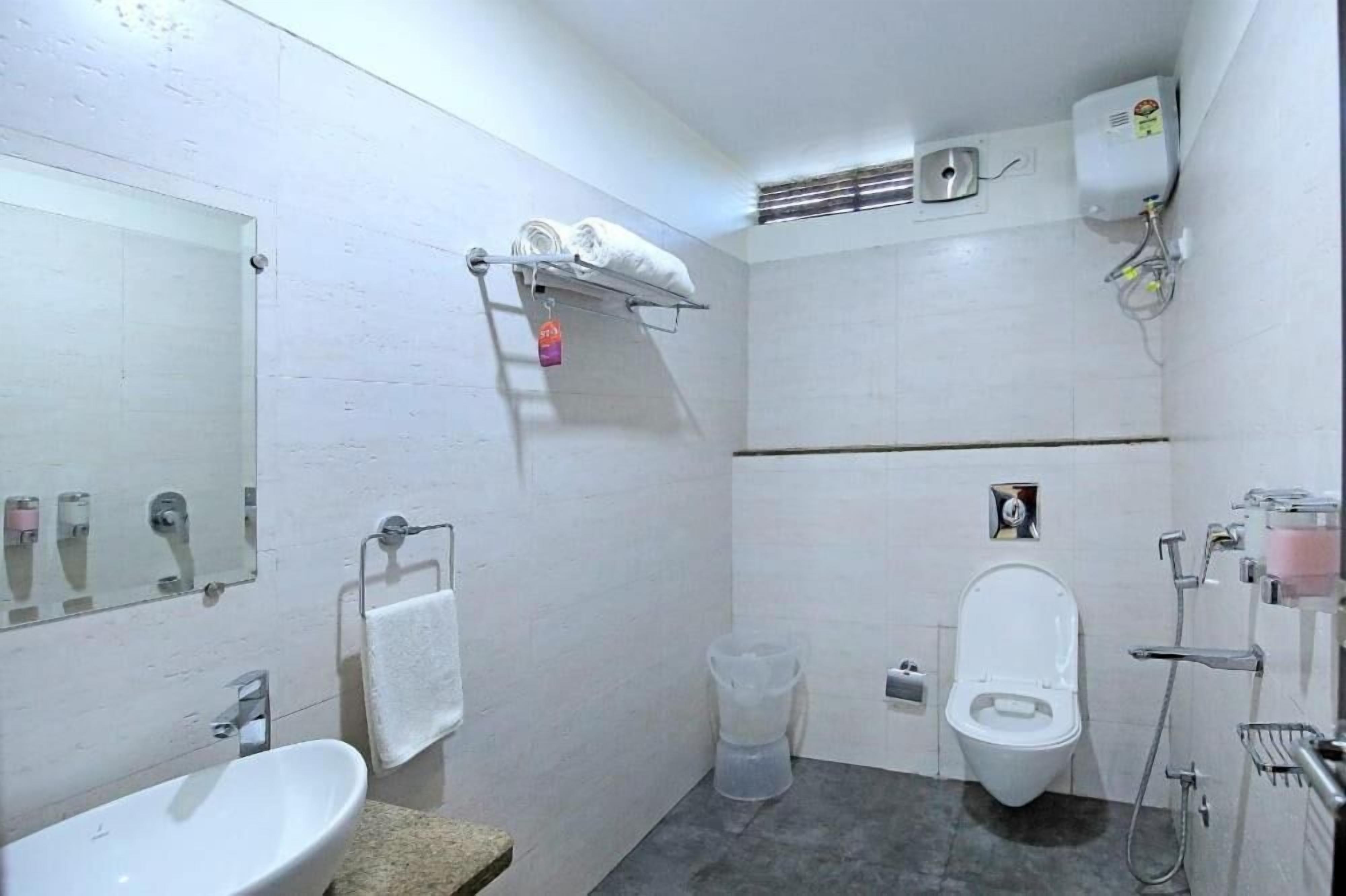 Une petite salle de bain moderne avec un lavabo, des toilettes et une douche, le tout de couleur blanche. On y trouve un porte-serviettes et une petite étagère avec des articles de toilette.