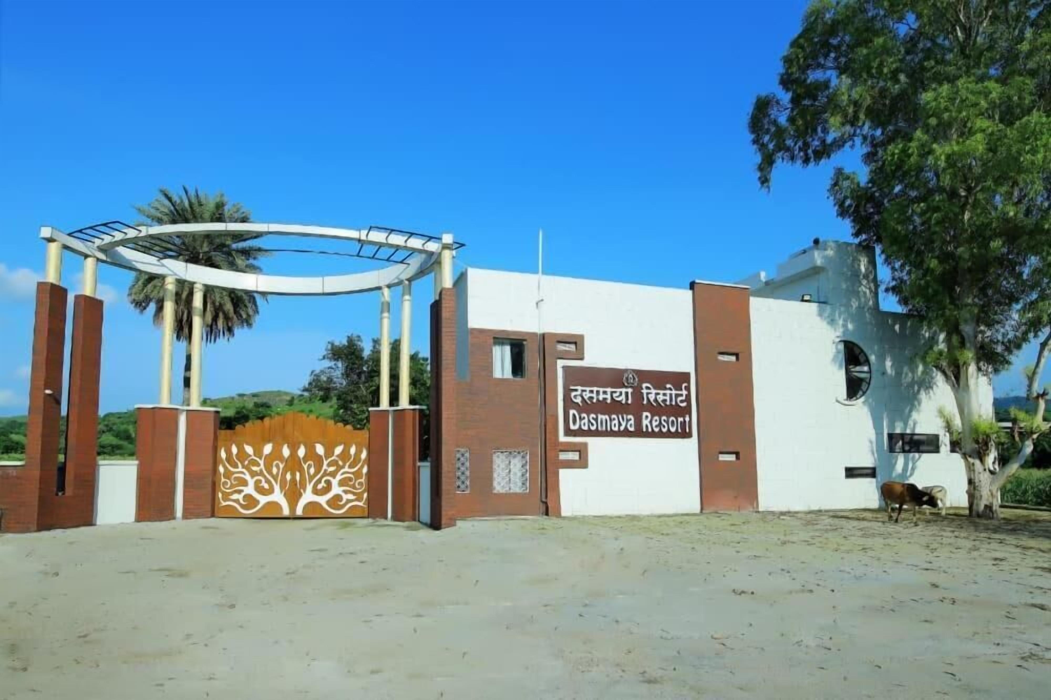 The entrance to Dasmaya Resort with a clear gate, a signboard, and a palm tree in the background.