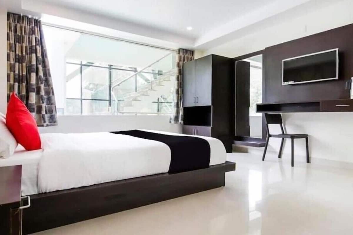 A modern hotel room with a large bed, a TV mounted on the wall, and a view of a building outside.