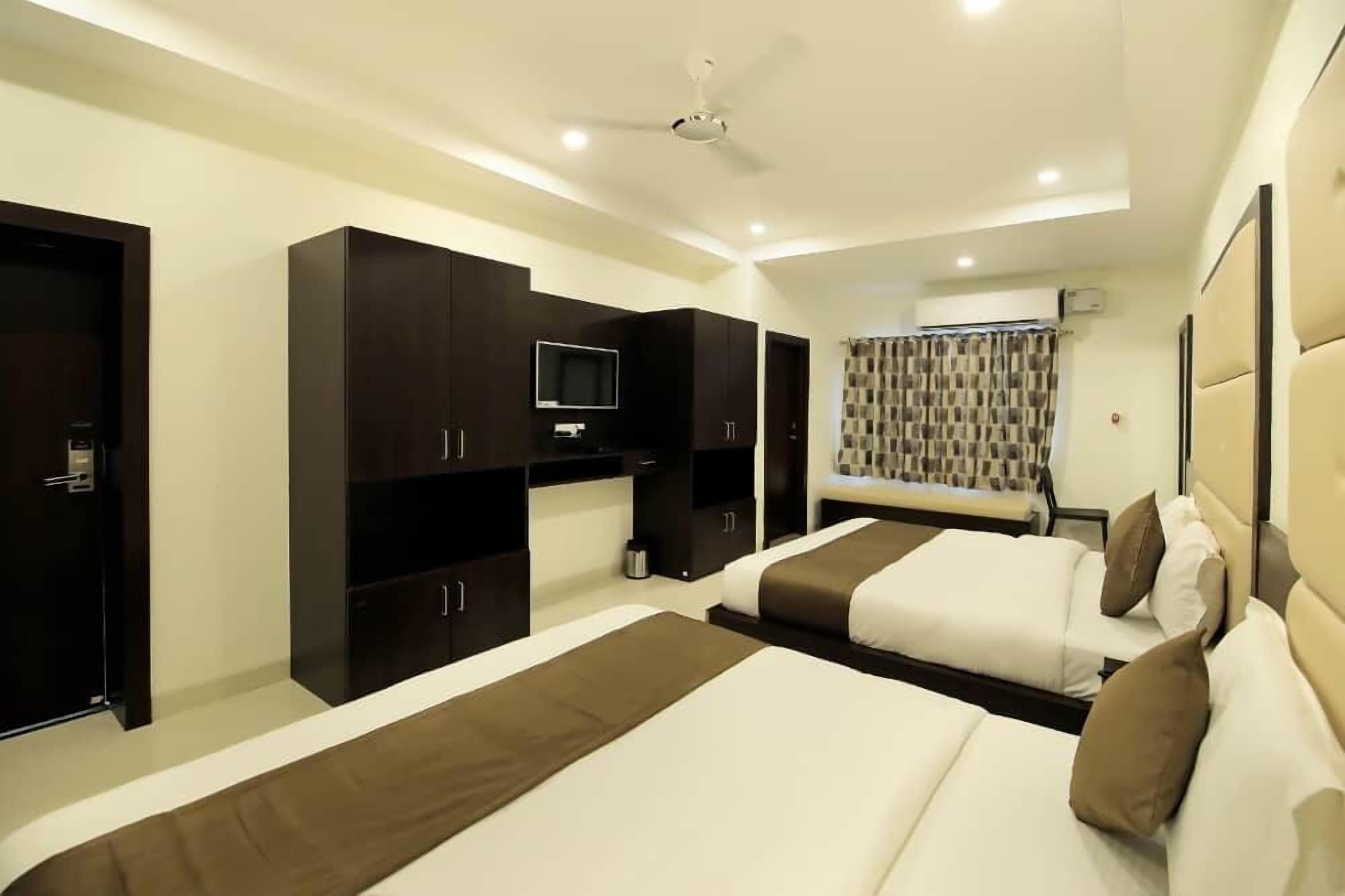 A hotel room with two beds, dark wooden wardrobes, a ceiling fan, and a television.