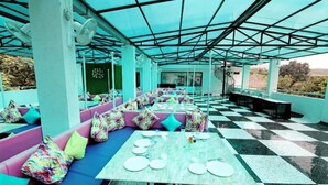 A covered outdoor seating area with checkered flooring, cushioned seating with colorful pillows, and tables set for dining. - Dasmaya Resort (Udaipur)