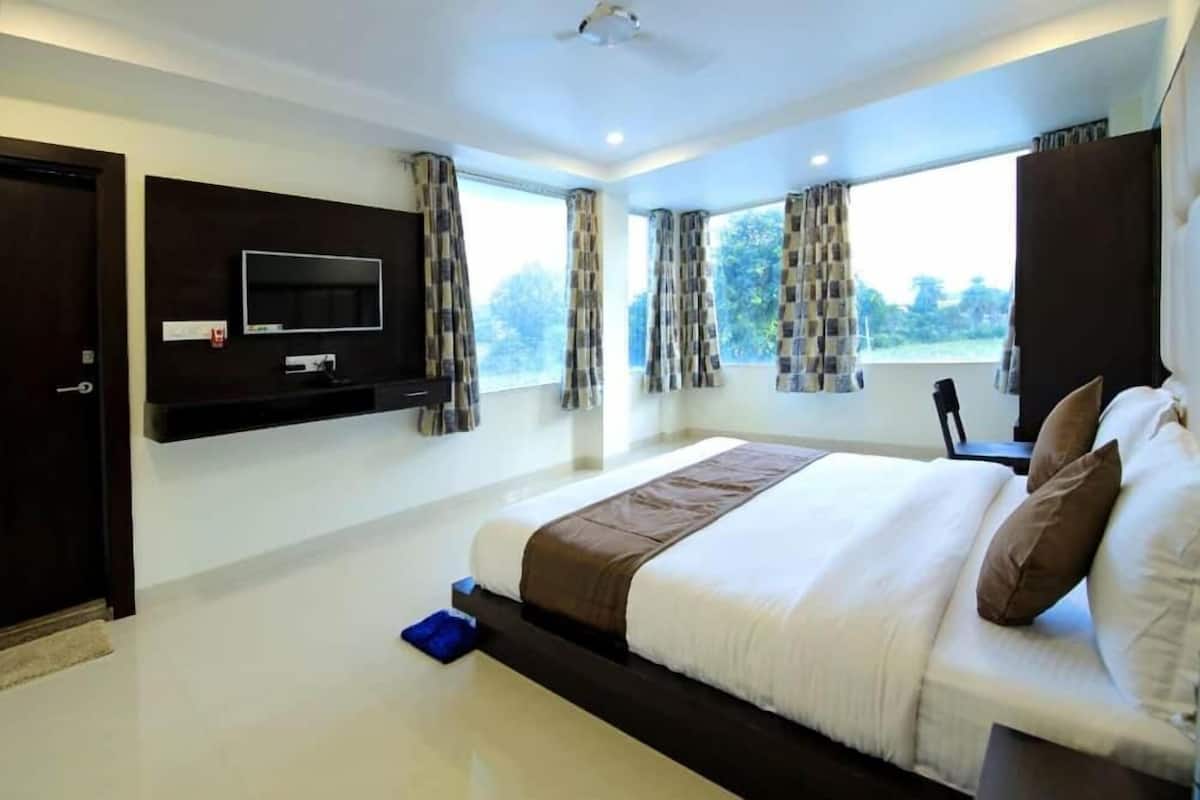A modern hotel room with a large bed, a mounted TV, and a view of the outdoors.