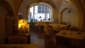 A dining area with tables and chairs, a window with curtains, and a tiled floor. - Hotel Garni (Isny im Allgaeu)