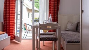 A room with a bed, a desk, and a chair. There is a window with curtains, and a view of the outside. - Hotel Garni (Isny im Allgaeu)