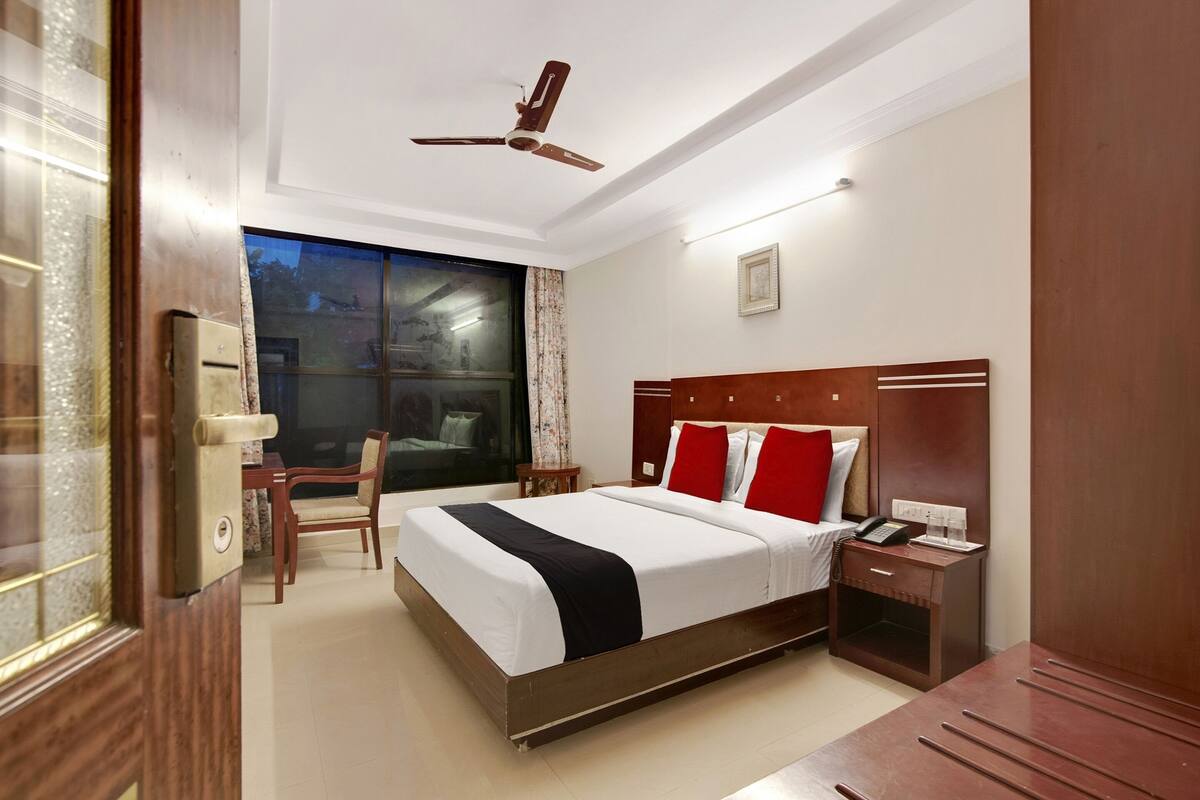 Une chambre d’hôtel avec un lit, une table de chevet, une commode et une fenêtre avec des rideaux.
