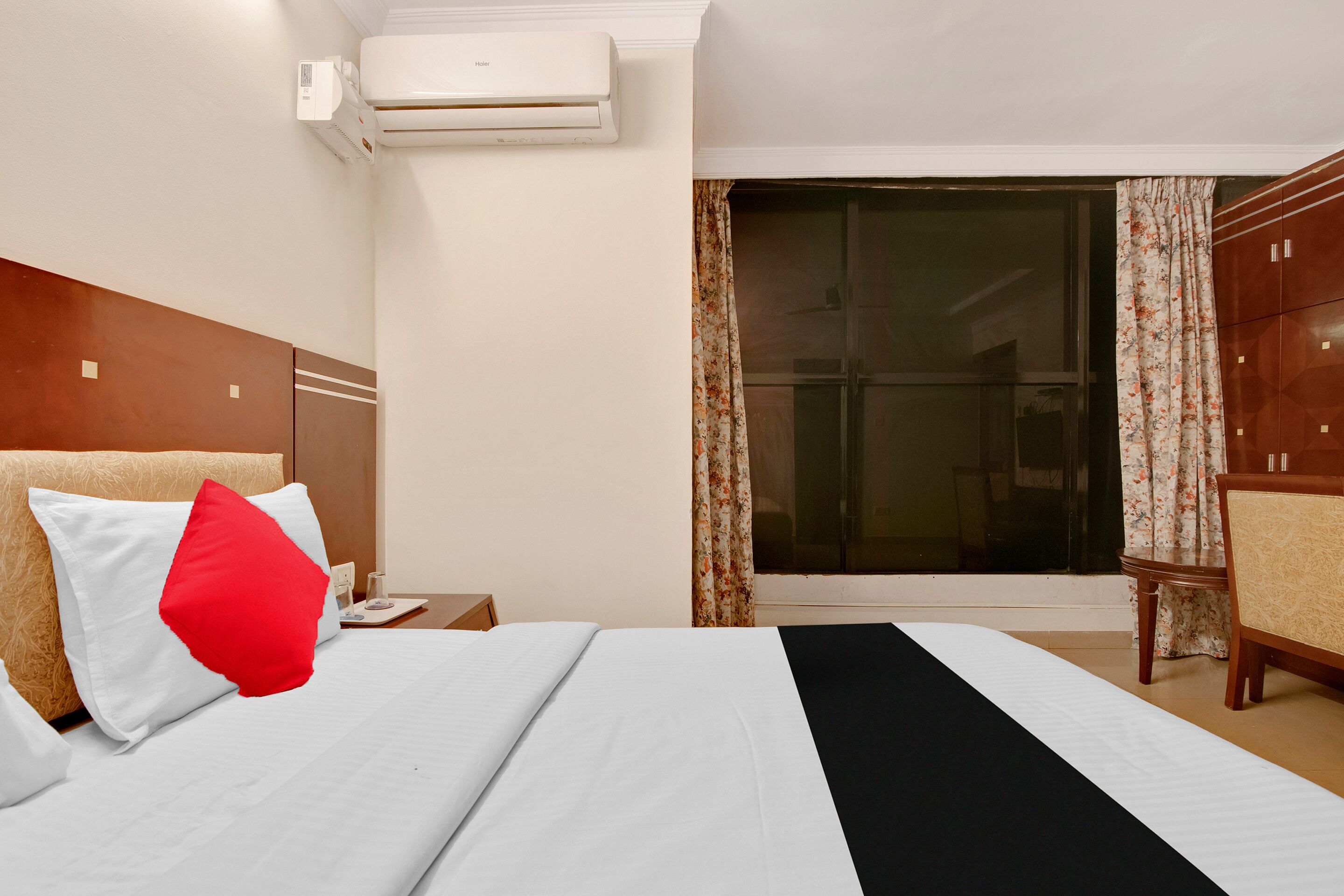A hotel room with a bed, a nightstand, an air conditioner, a wardrobe, and a sliding glass door to a balcony.