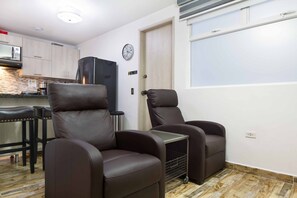 A compact living space with two reclining chairs, a small kitchen area, and a clock on the wall.