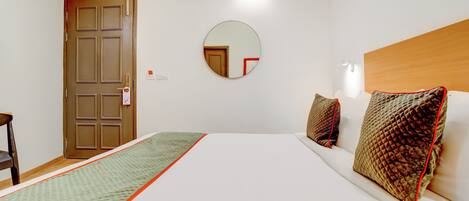 Habitación de hotel con cama, espejo redondo, puerta de madera y aire acondicionado instalado en la pared.