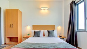 A hotel room with a bed, wooden wardrobe, bedside table, lamp, and a window with curtains. - Hotel Aravali Inn & Banquet Hall (Faridabad)
