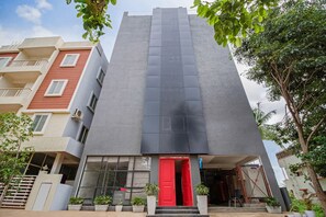 A modern building with a red door, large windows, and potted plants.