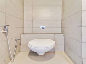 A small, tiled bathroom with a toilet, a shower, and a wall-mounted faucet.