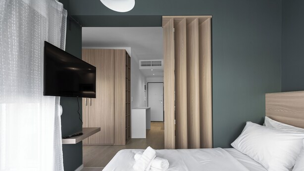 A modern hotel room with a bed, a TV mounted on the wall, and a wooden wardrobe. - DeniZen Boutique Apartments, Nilie Hospitality MGMT (Thessaloniki)
