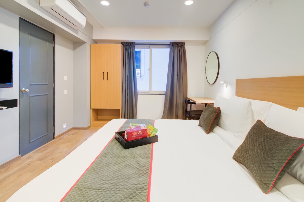 A hotel room with a bed, a TV, a desk, and a window with curtains.
