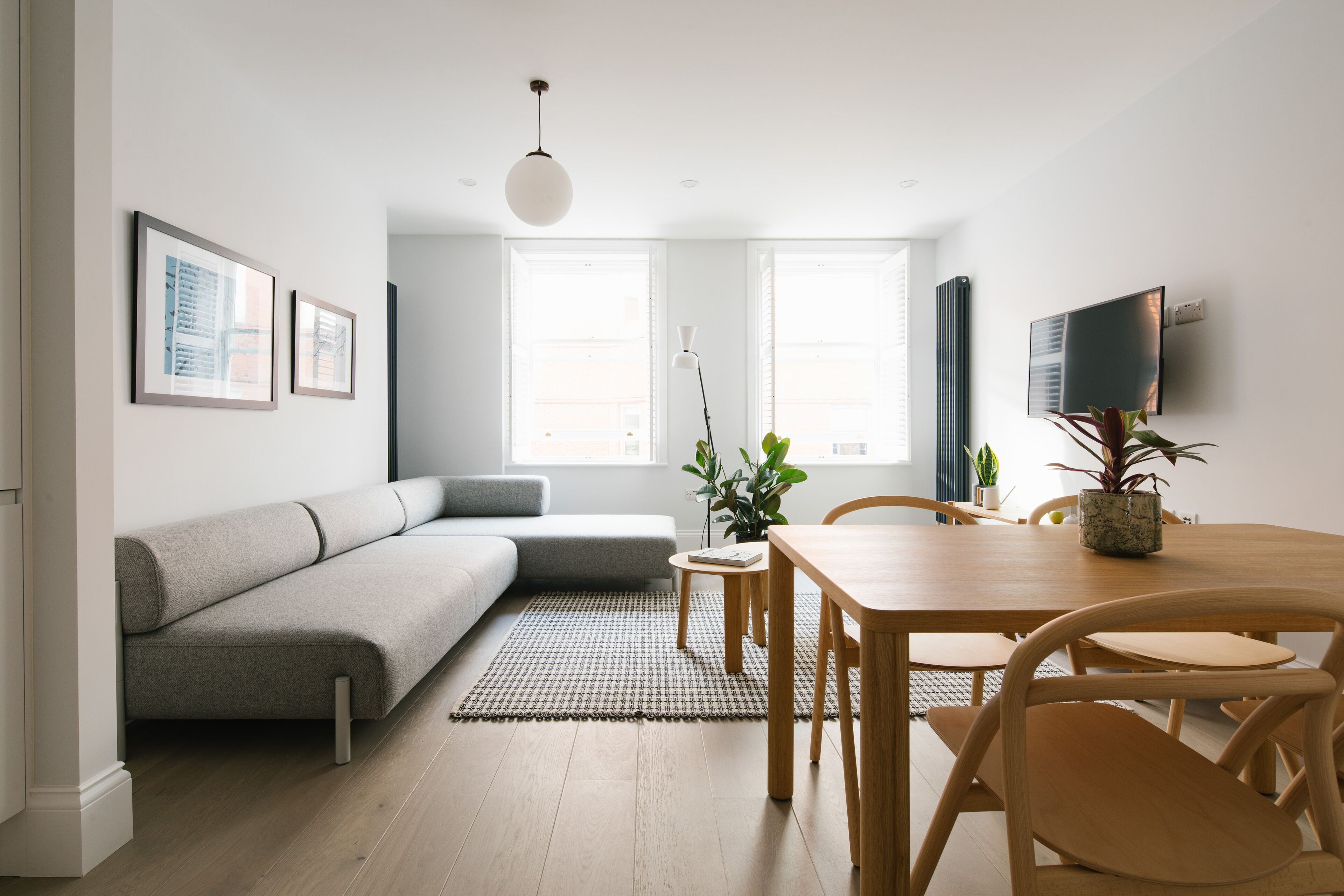 A modern living room with a grey sofa, a wooden dining table with chairs, a small rug, and a potted plant.