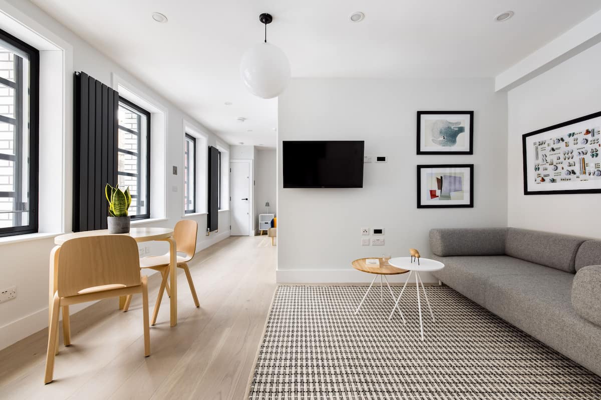 A modern living room with a grey sofa, wooden chairs, a small round table, and a TV mounted on the wall.