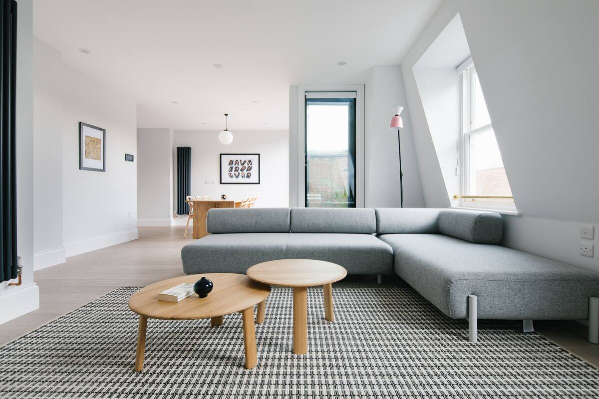 A modern living room with a grey sectional sofa, two wooden coffee tables, a patterned rug, and a large window with a view.