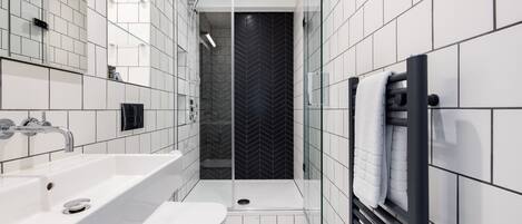 A modern bathroom with a white sink, toilet, and shower area, featuring a black herringbone-patterned wall and a glass shower enclosure.