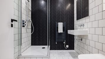 A modern bathroom with a glass-enclosed shower, a white sink, and a black tiled wall with a chevron pattern.