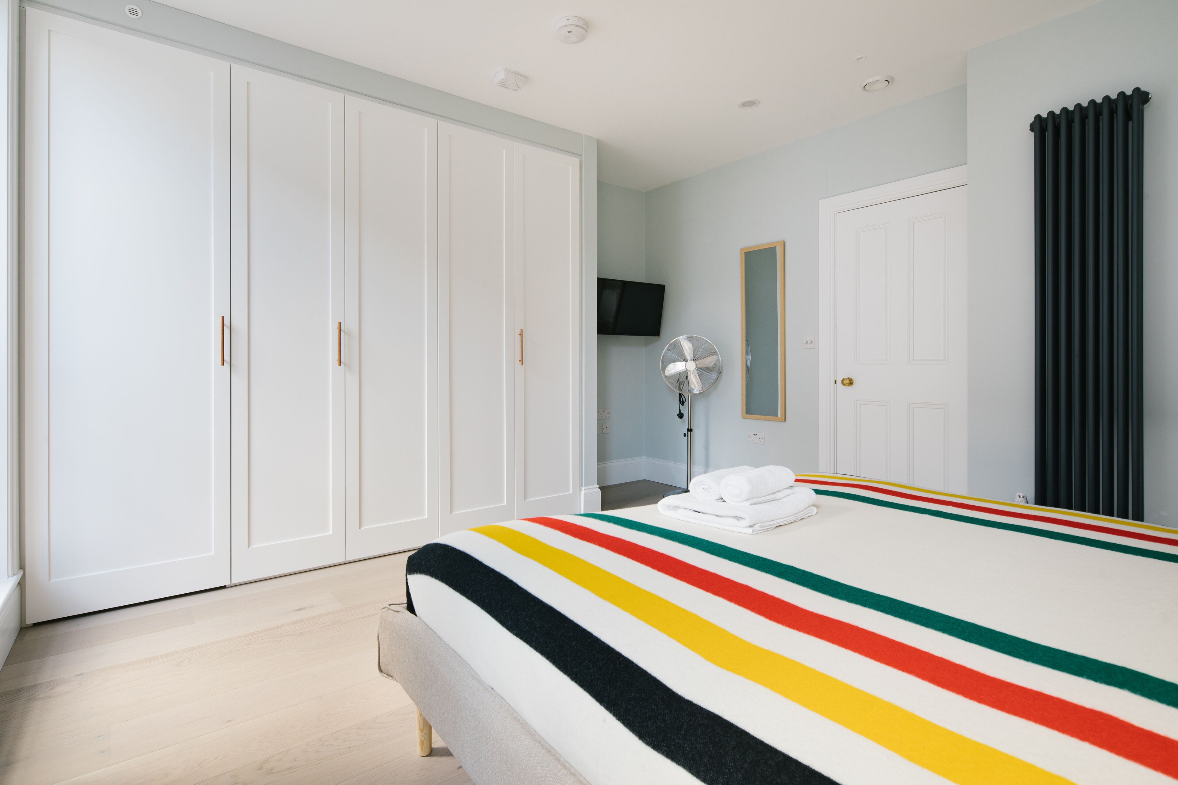 Una camera da letto con un letto grande, un'armadio bianco, una TV a schermo piatto e un termosifone.