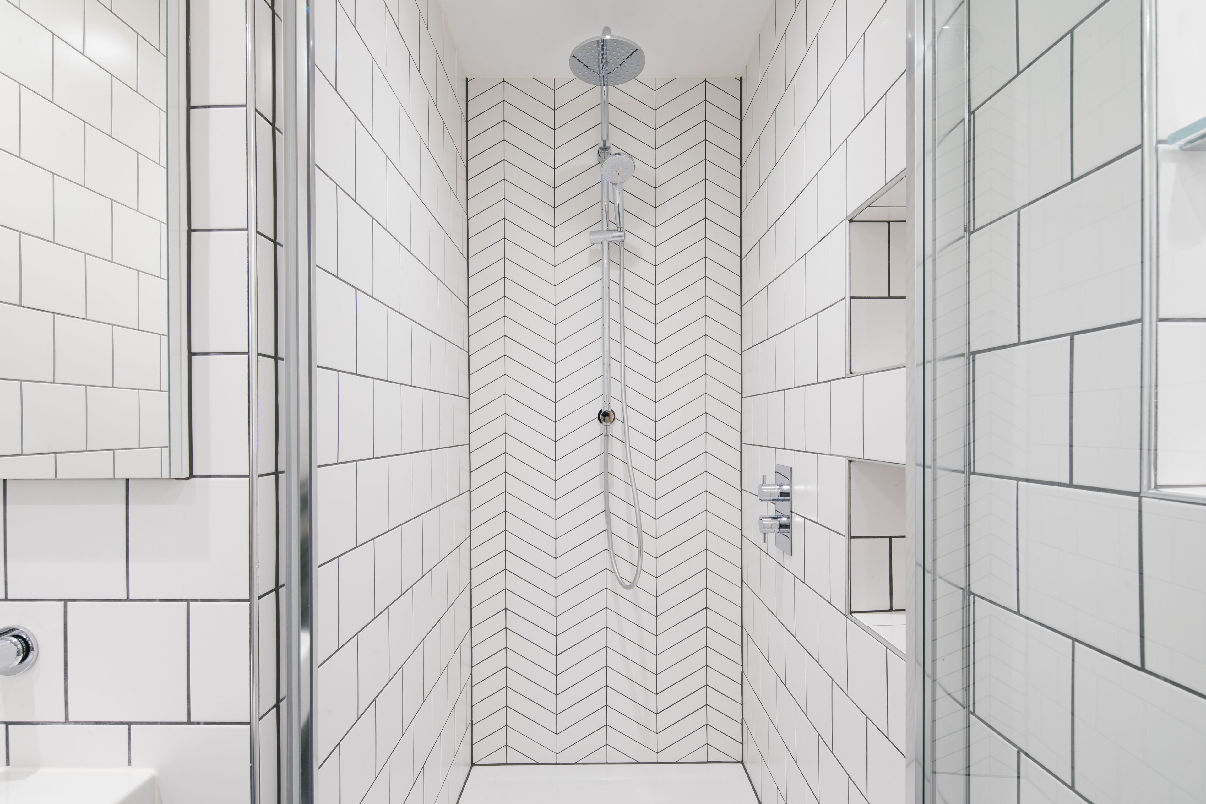 A modern shower with a chevron tile pattern, a glass door, and a chrome showerhead.