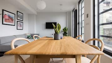 A modern living room with a wooden dining table, grey sofa, and large windows.