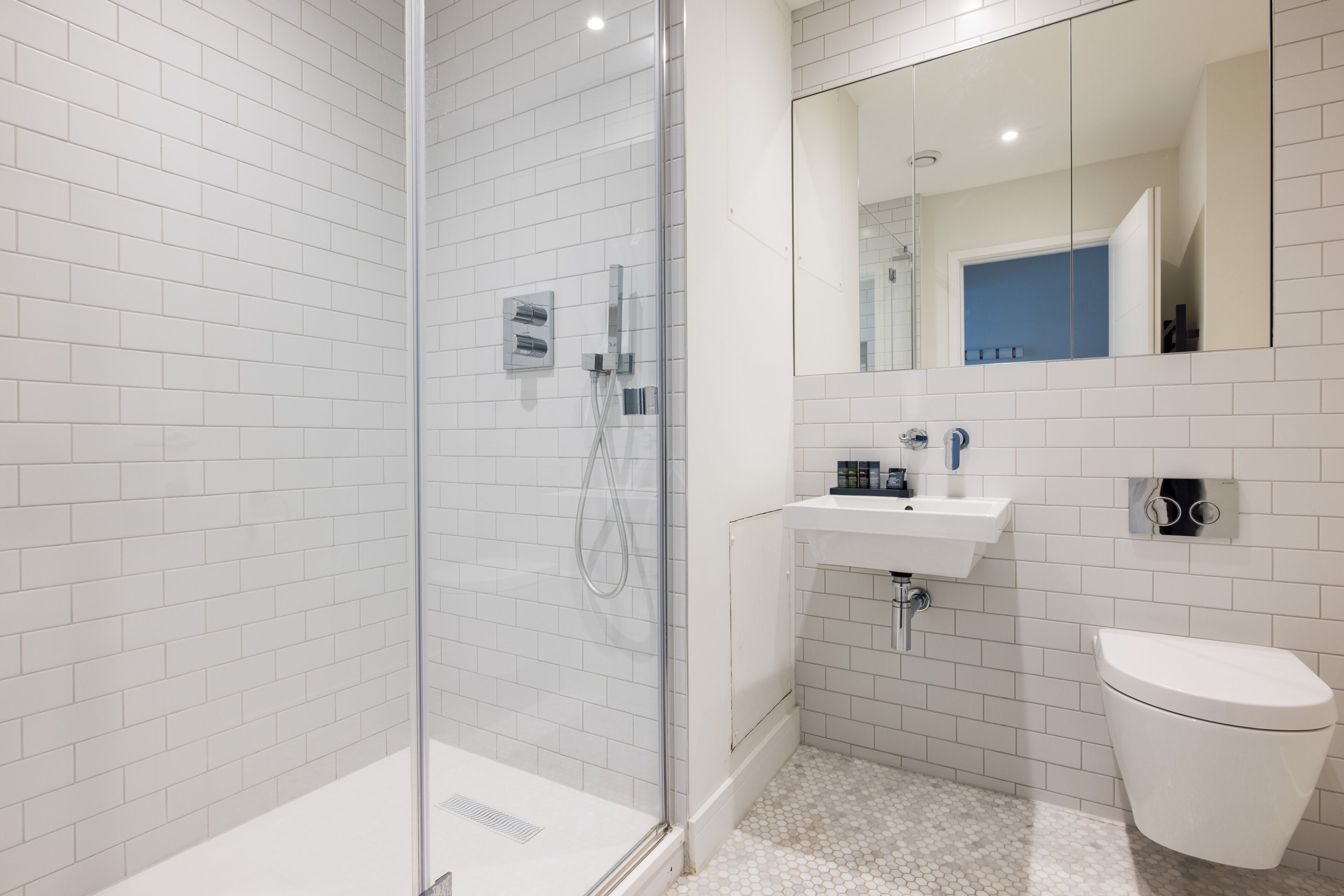 A modern bathroom with white subway tiles, a glass shower enclosure, a white sink, and a toilet.