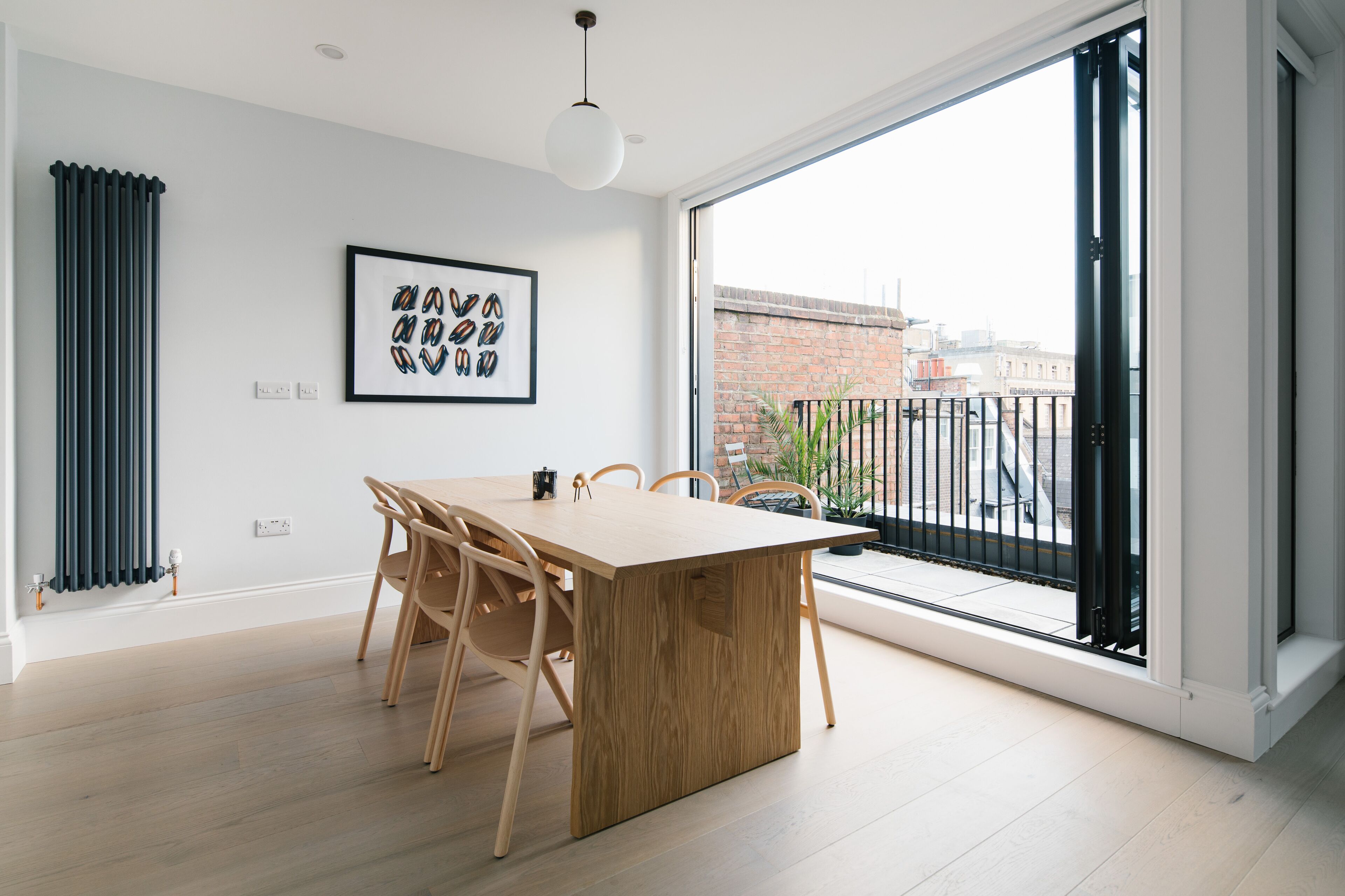 Un comedor moderno con una mesa y sillas de madera, un cuadro enmarcado en la pared, y vistas de la ciudad a través de amplias ventanas.
