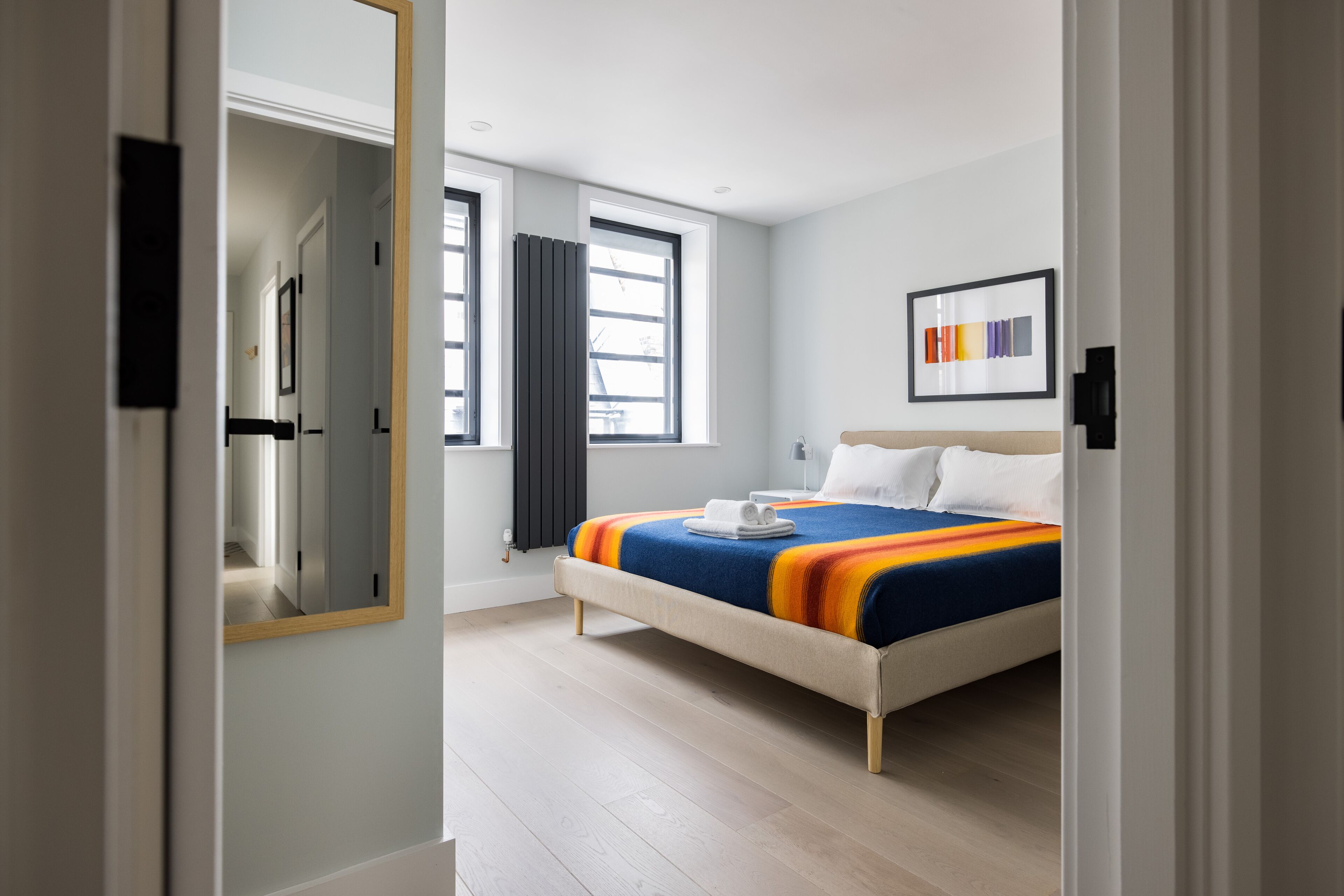 Une chambre d’hôtel moderne avec un grand lit, une table de chevet, un miroir et une fenêtre avec des rideaux.