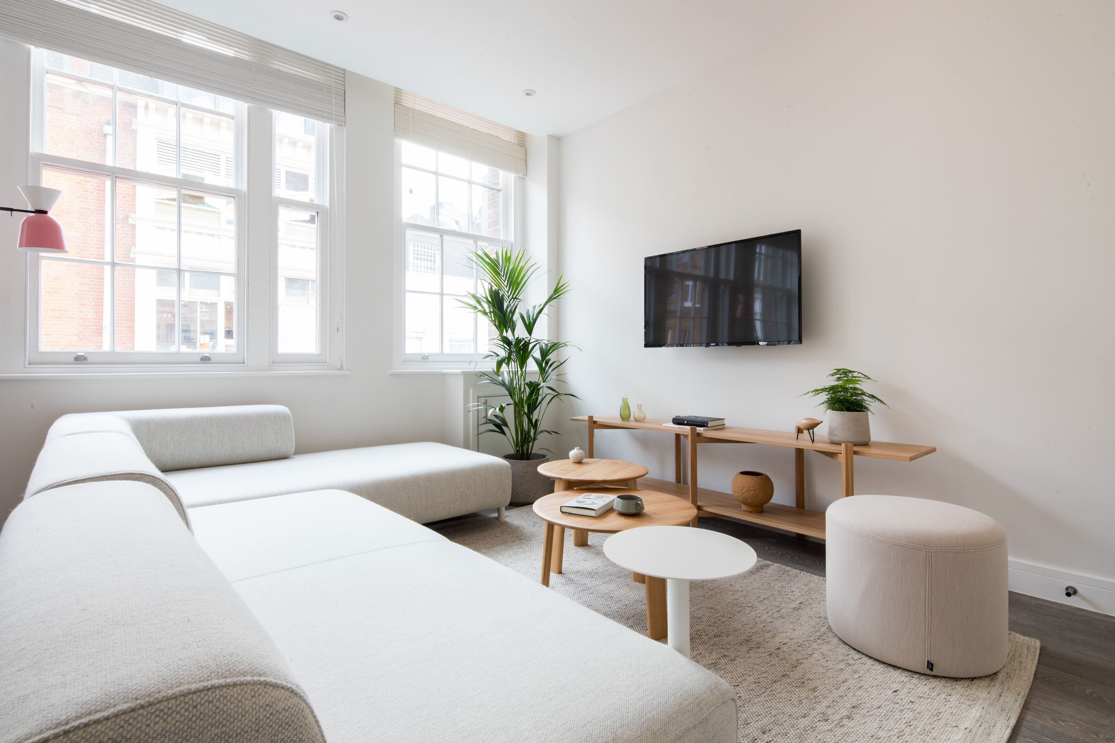 A modern living room with a large sofa, a coffee table, a small round table, and a TV mounted on the wall.
