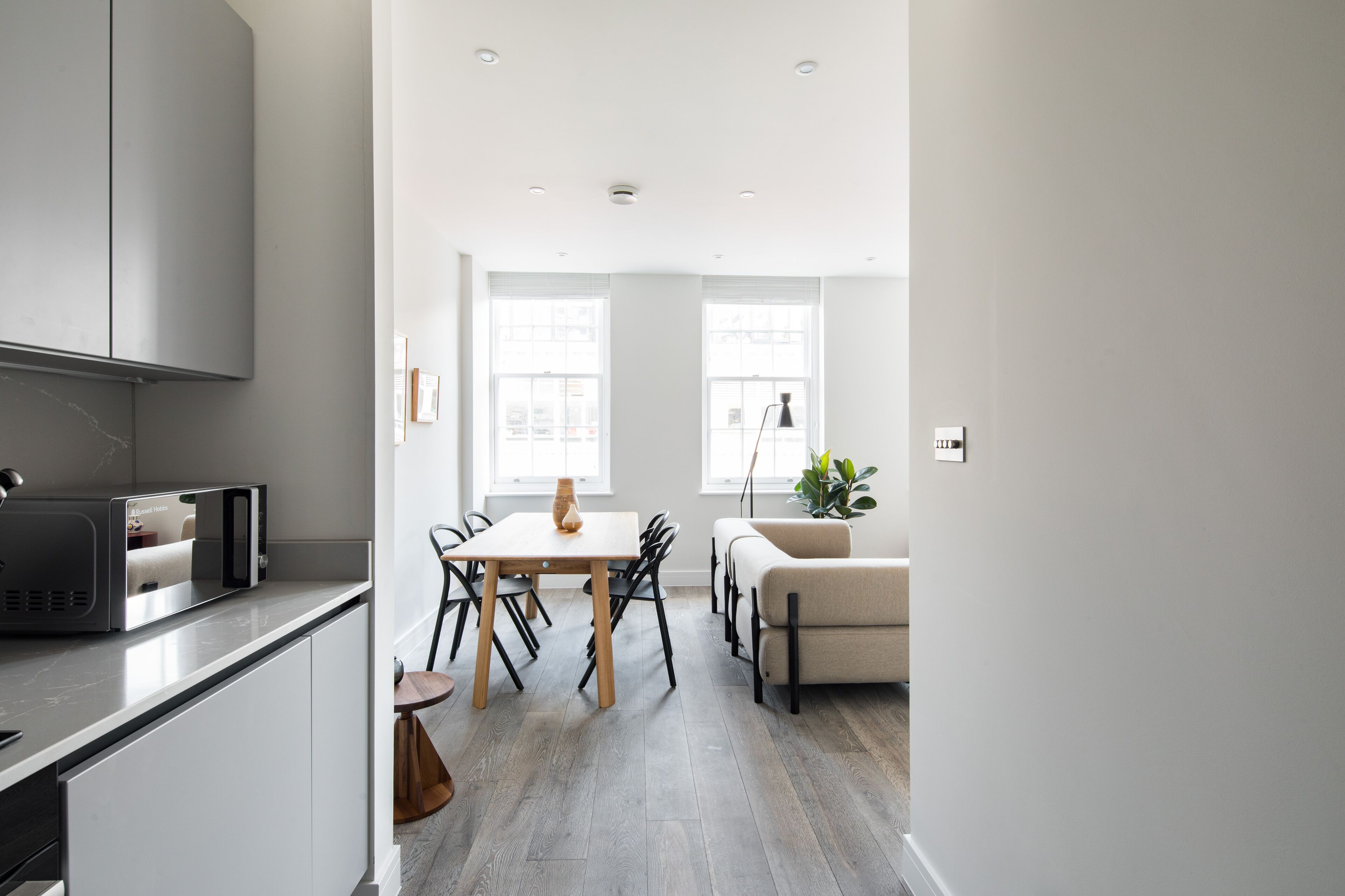 A modern kitchen with a built-in microwave, a dining area with a table and chairs, and a sofa in the background.