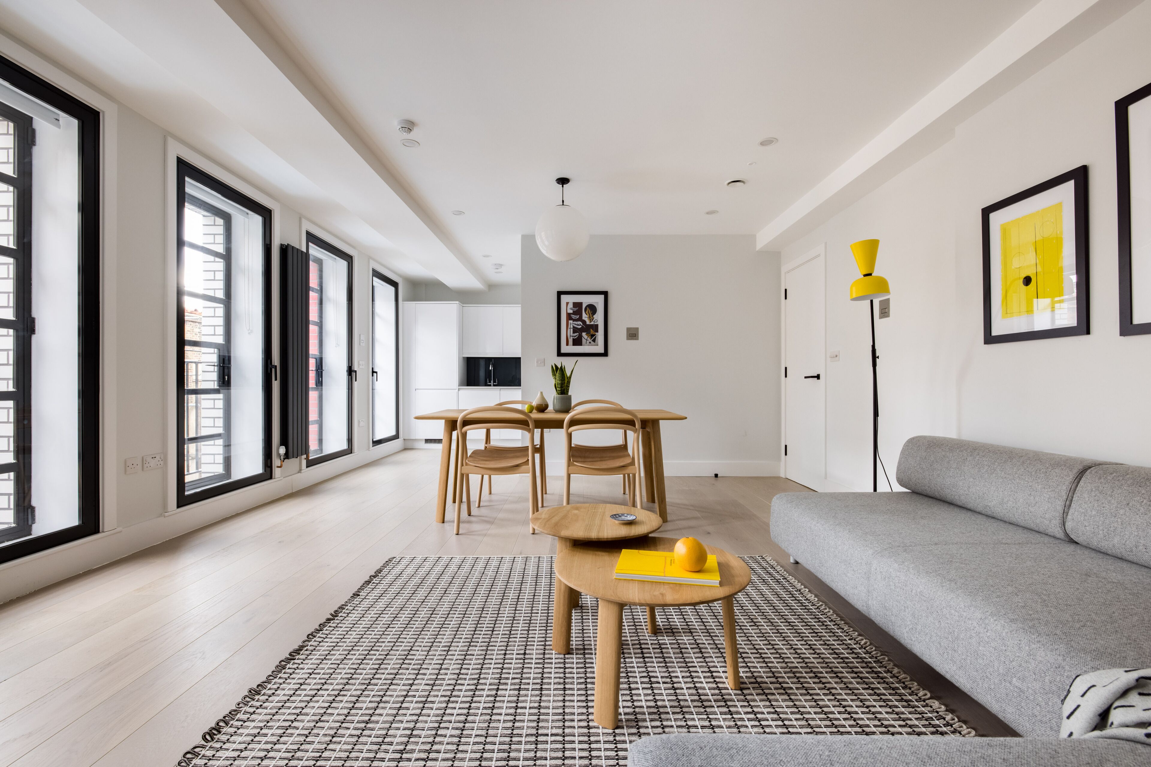 A modern living room with a grey sofa, a wooden dining table with chairs, and a patterned rug.