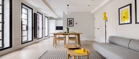 A modern living room with a grey sofa, a wooden dining table with chairs, and a patterned rug.