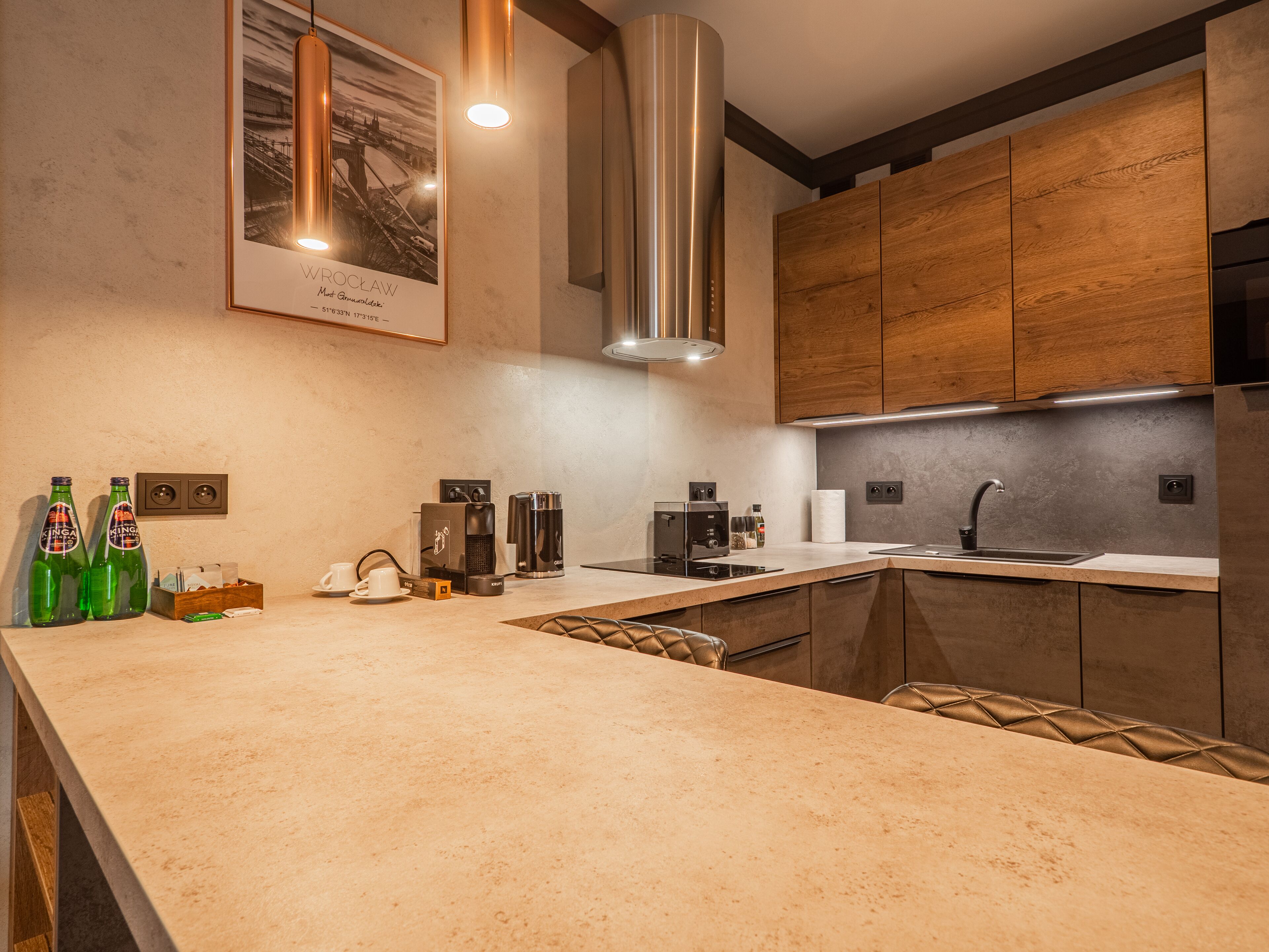 Una cocina moderna con una isla grande, electrodomésticos de acero inoxidable, armarios de madera y un cuadro en la pared.