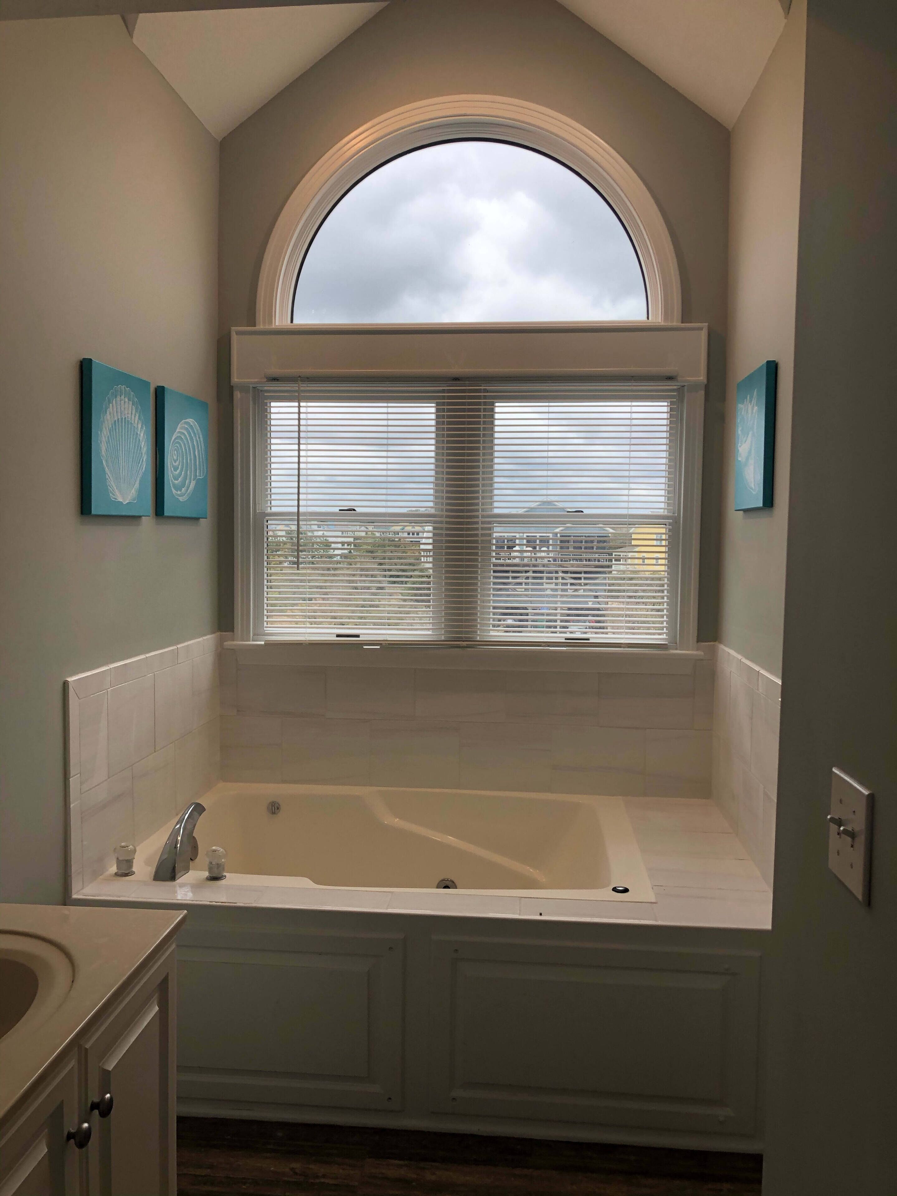 Un baño con una bañera independiente, una ventana con persianas y dos obras de arte colgadas en la pared.