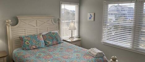 A bedroom with a bed, a nightstand, a lamp, and a window with blinds.