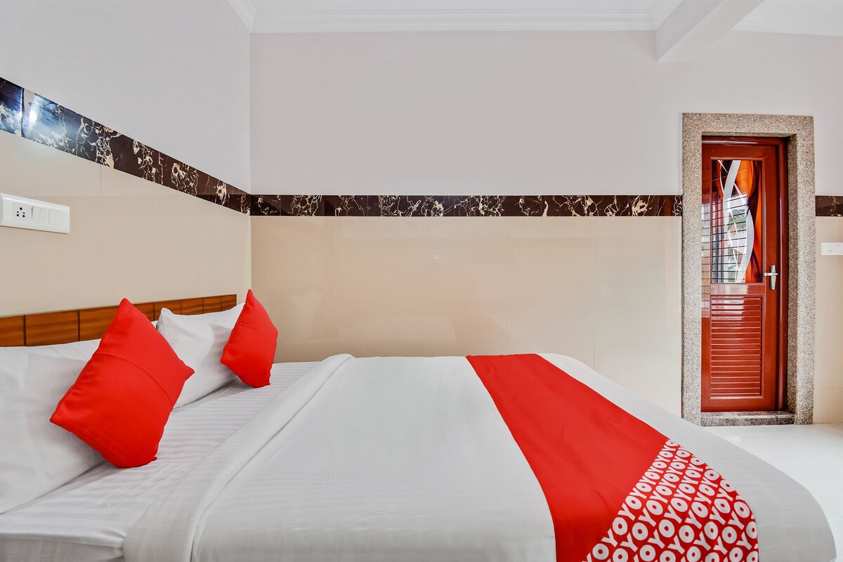 A hotel room with a bed, red and white bedding, a patterned throw, and a door with a window.