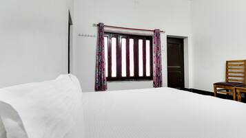 A hotel room with a bed, a window with curtains, a wooden chair, and a door.