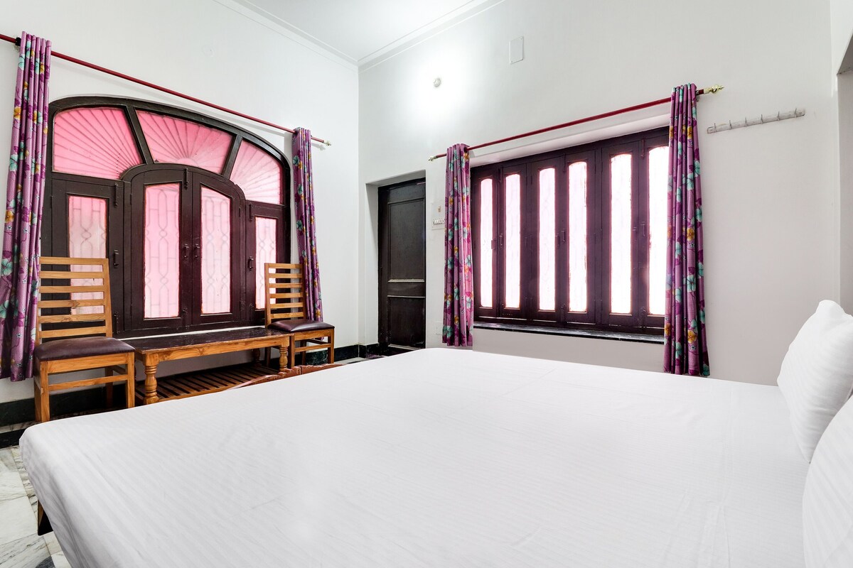 A bedroom with a large bed, two wooden chairs, a bench, and a window with curtains.