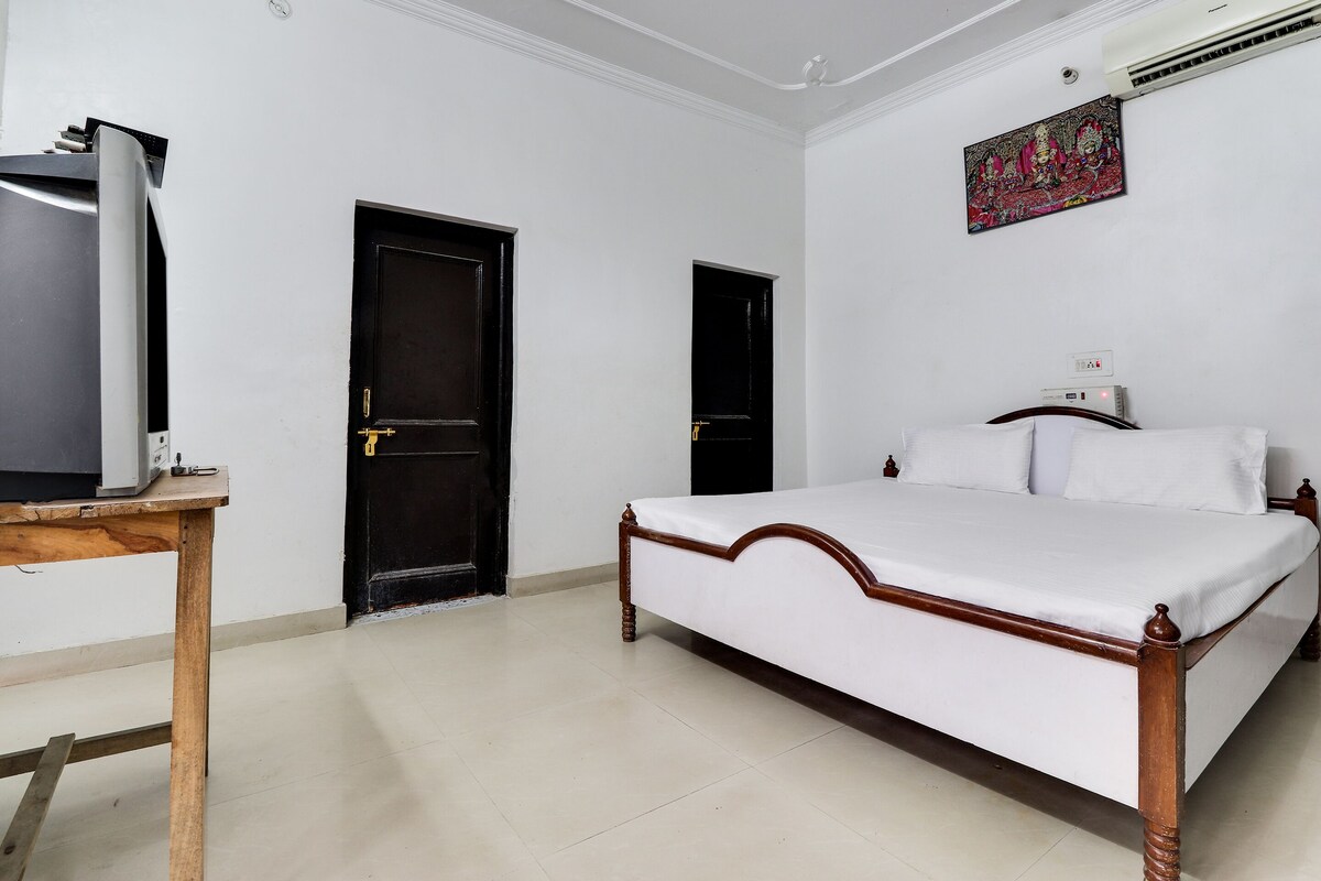 A bedroom with a bed, two doors, a TV on a stand, and an air conditioner.