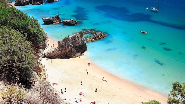 Une plage aux eaux turquoise et limpides, parsemée de rochers et où sont amarrés plusieurs bateaux.