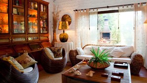 Un salon chaleureux, avec des meubles en osier, une cheminée et une vue sur la verdure environnante.