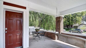Un patio techado con pared de ladrillo, una puerta roja y una mesa con sillas.