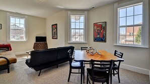 Una habitación con una mesa de comedor, sillas, un sofá negro, un televisor y obras de arte en las paredes.