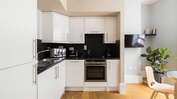 Cocina moderna con armarios blancos, encimera negra y horno. Hay una planta y una silla en la habitación.